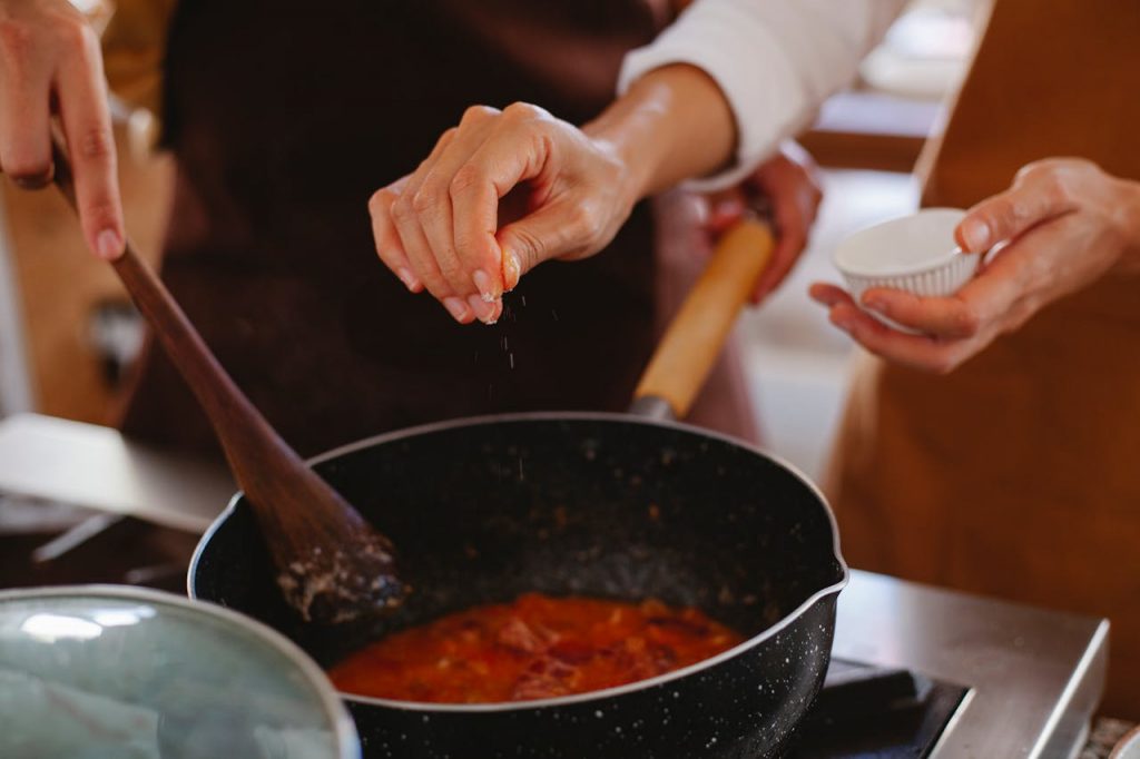Close-up of hands seasoning a dish in a pot, creating a homemade culinary masterpiece.