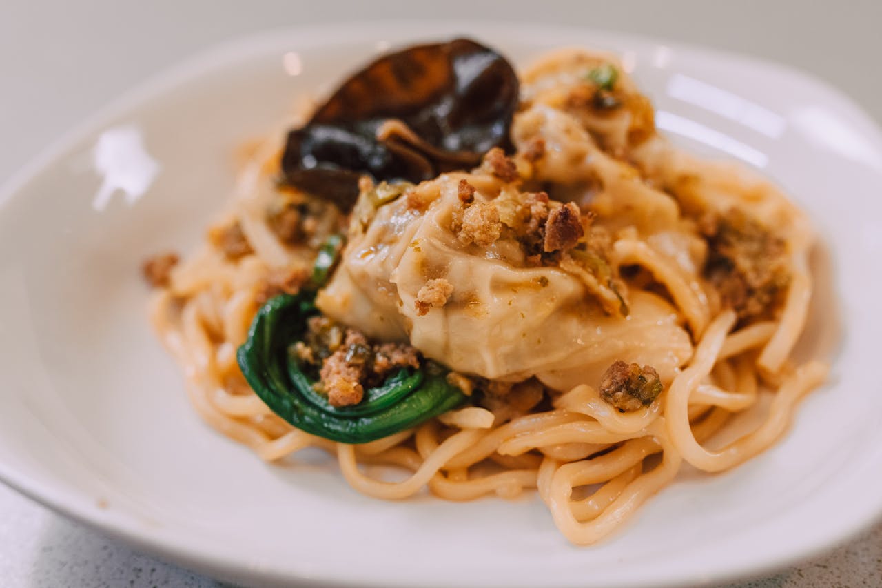 A delicious Asian noodle dish topped with dumplings and garnished on a plate.